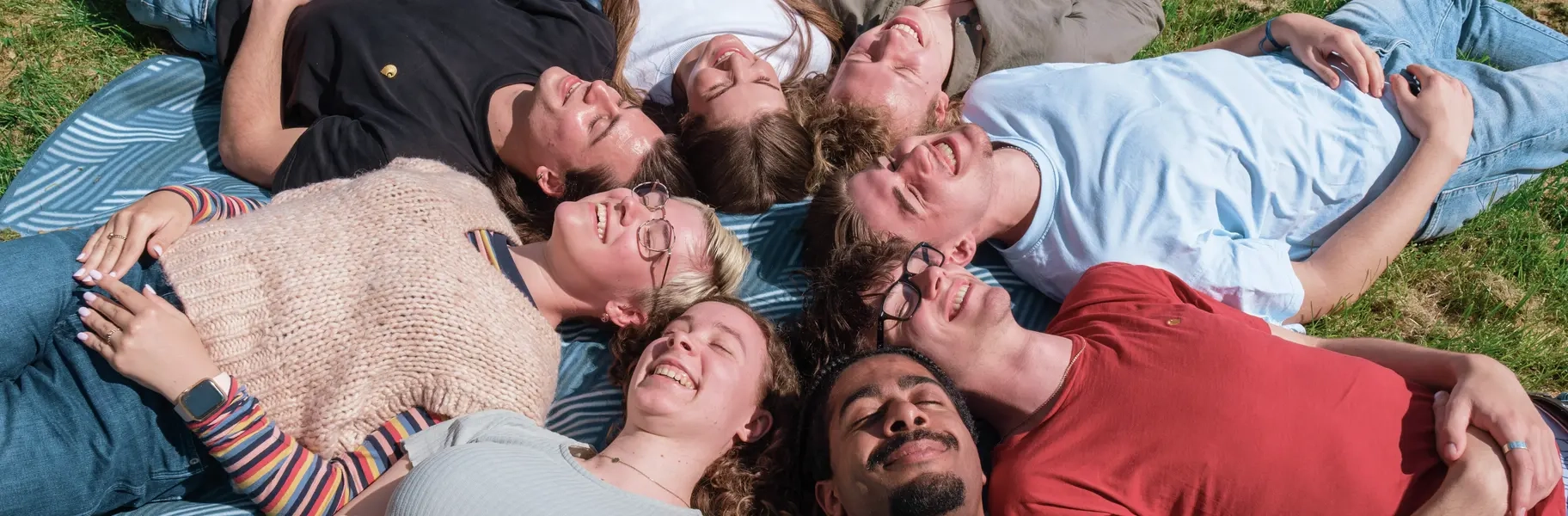 Junge Menschen liegen im Kreis auf einer Wiese, die Köpfe zusammen